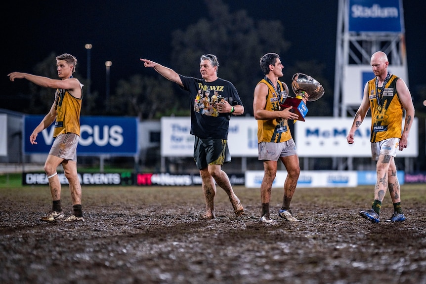 four men standing in mud on an oval.