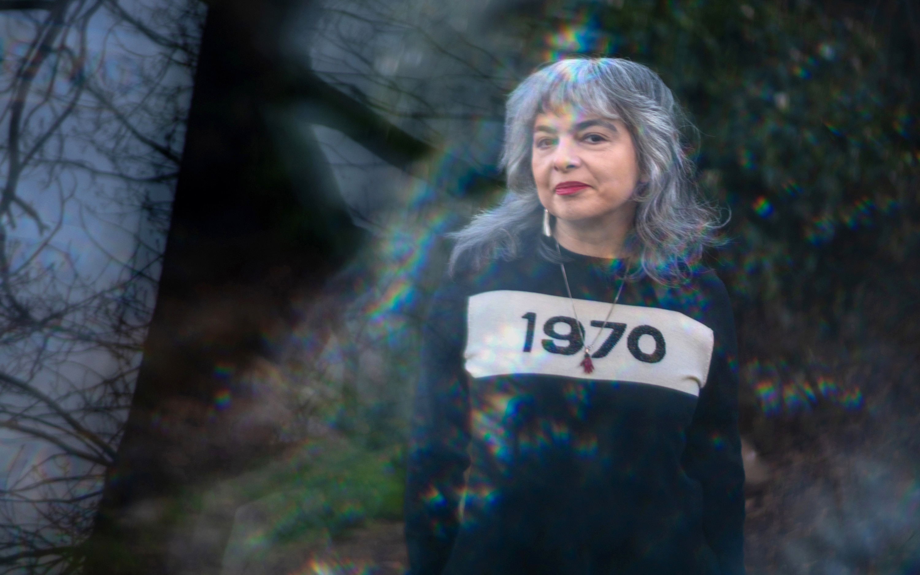 A woman with silver hair is seen through a glass prism in a jumper with "1970" printed on the front.