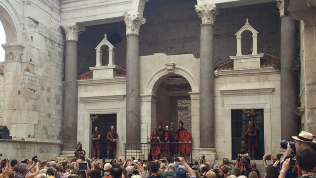 A crowd of tourists with cameras out watch a re-enactment of soldiers as they address the crowds