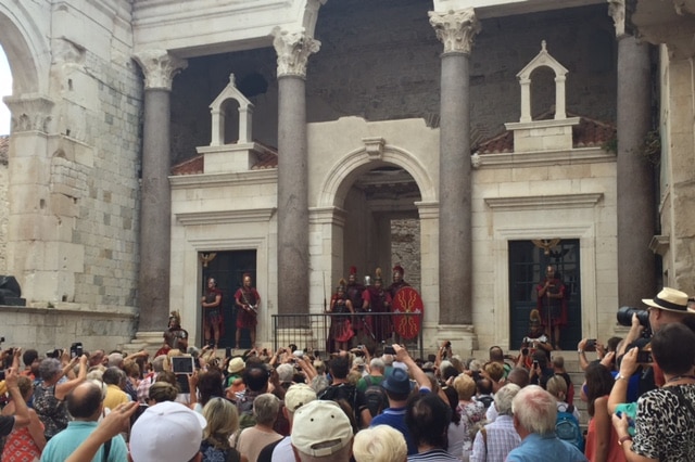 A crowd of tourists with cameras out watch a re-enactment of soldiers as they address the crowds