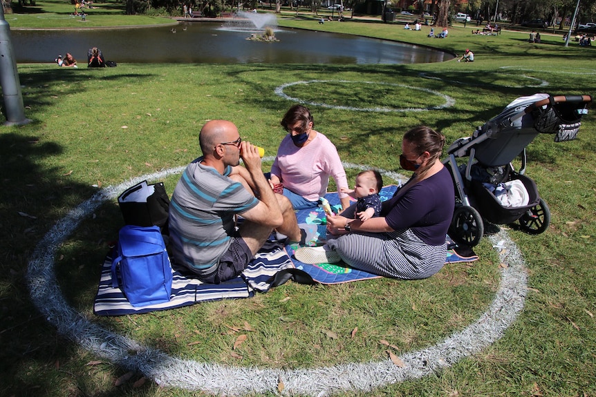 A family sits on the grass within an allocated space marked out on the ground