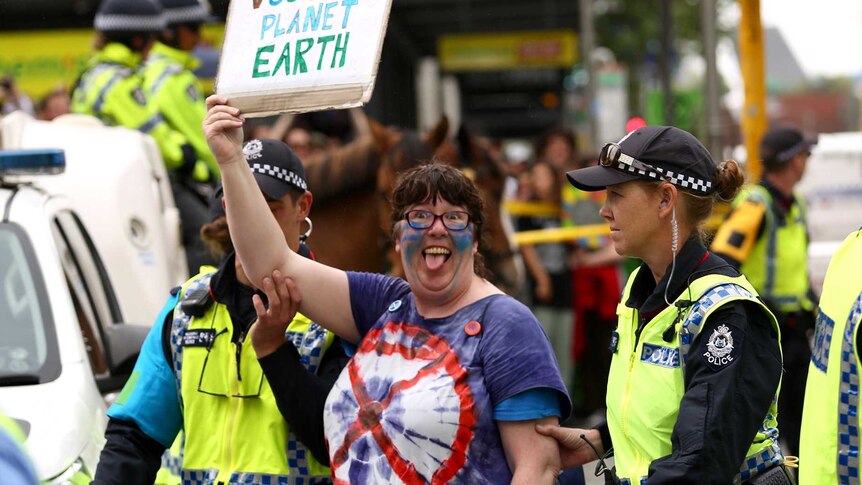 An Extinction Rebellion protester being arrested by police holding up a protest sign.