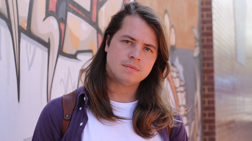 Craig Campbell stands in front of a wall covered in graffiti.