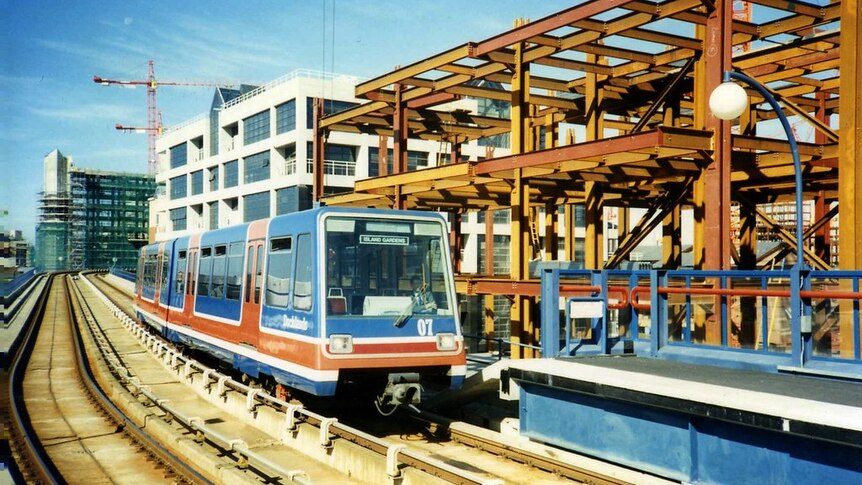 A red white and blue light rail vehicle travels down an elevated rail track past bright bronze scaffolding.