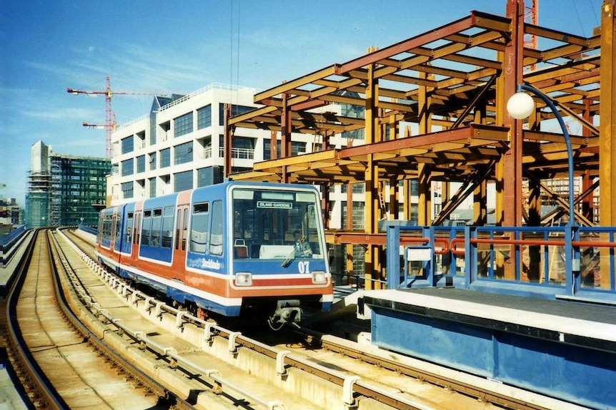 A red white and blue light rail vehicle travels down an elevated rail track past bright bronze scaffolding.