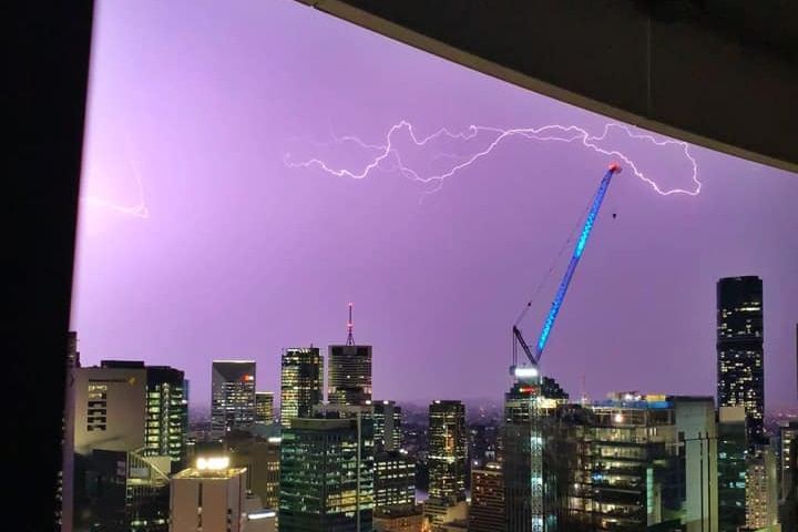 Lightning seen from window over the city skyline, near a crane.