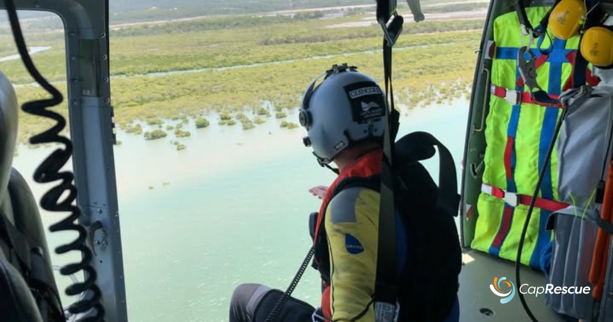 Una persona sentada en el borde de un helicóptero contempla un paisaje inundado.