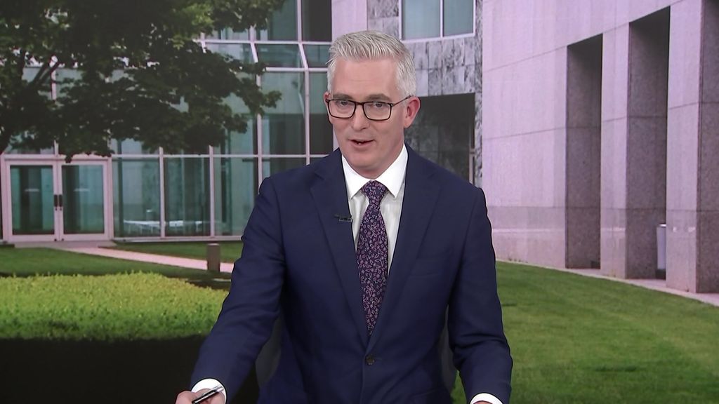 A grey-haired man with glasses in a suit and tie speaking in a TV studio against the greenscreen backdrop of a courtyard.