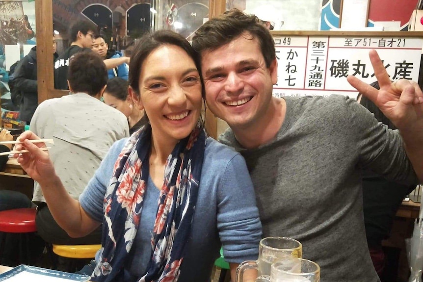 A man and a woman smiling, sitting at a table with sushi and beer on it in a japanese restaurant.