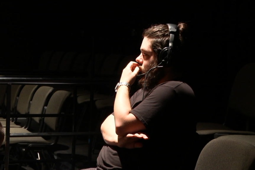 William Yates sitting in a row of theatre seats with a headset and microphone on