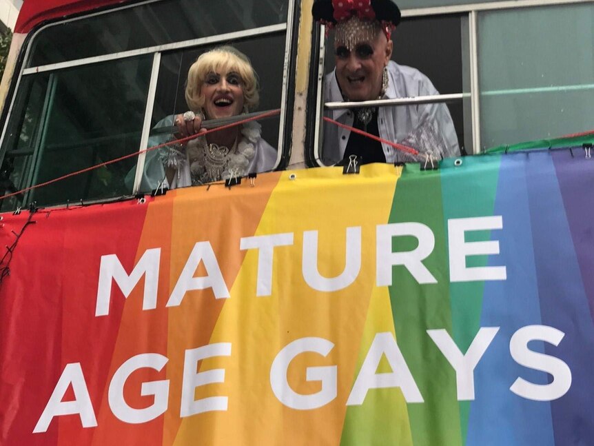 Two people hang a rainbow "Mature Age Gays" sign from their float for Mardi Gras Sydney.