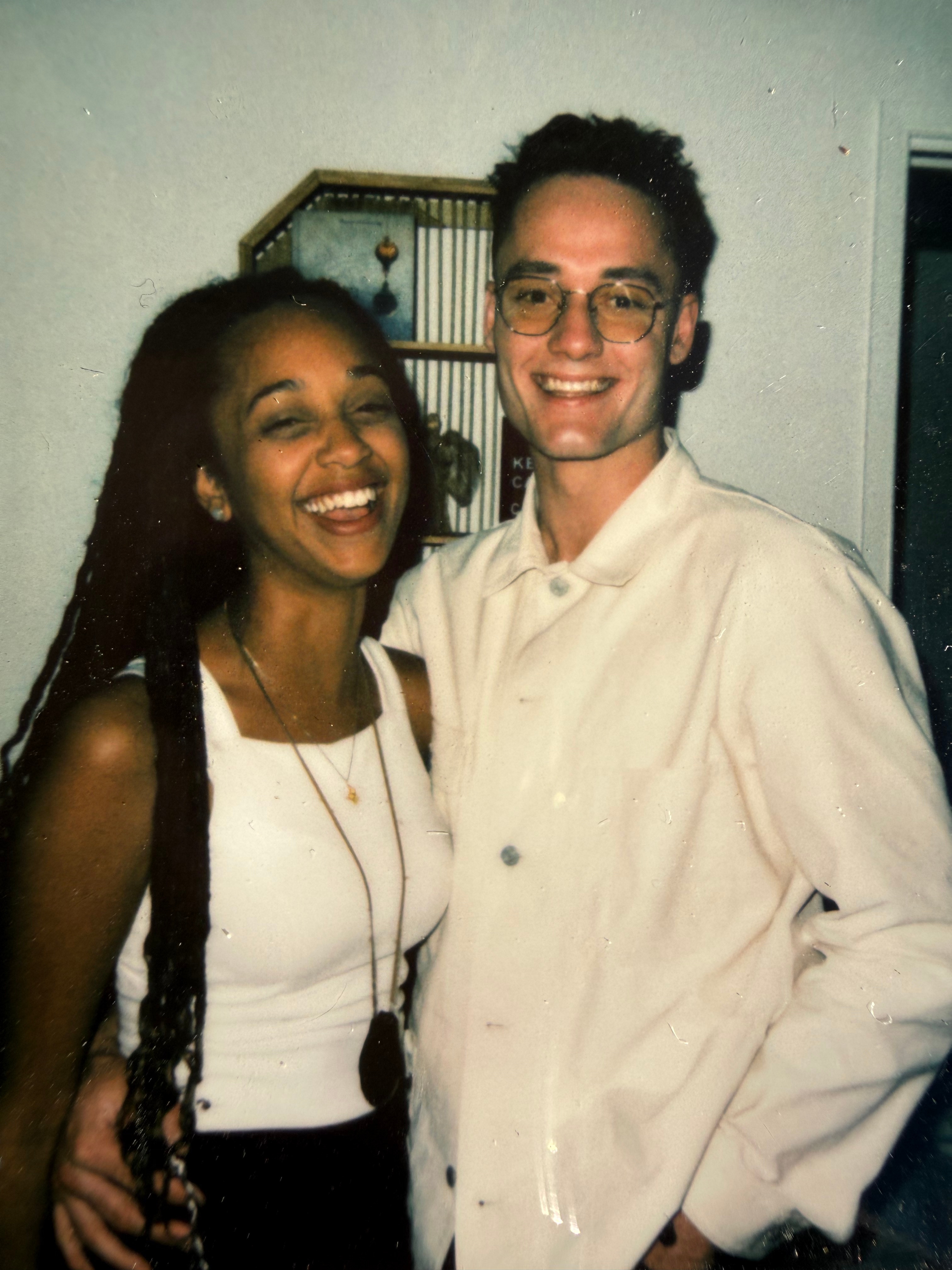 A young dark-skinned woman with long hair stands next to a tall young white man. They are both smiling. 