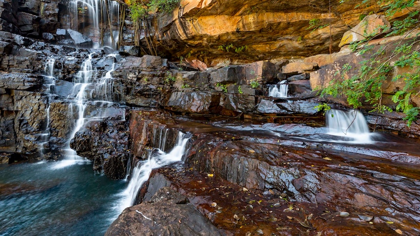 A waterfall runing down a rock face, with a pond on the left.