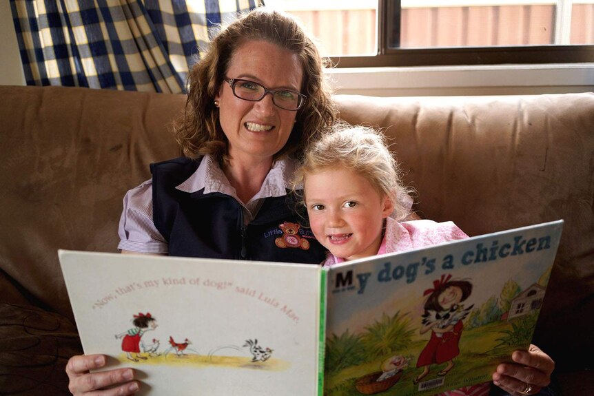 A woman and her young daughter sitting on a couch with a story book