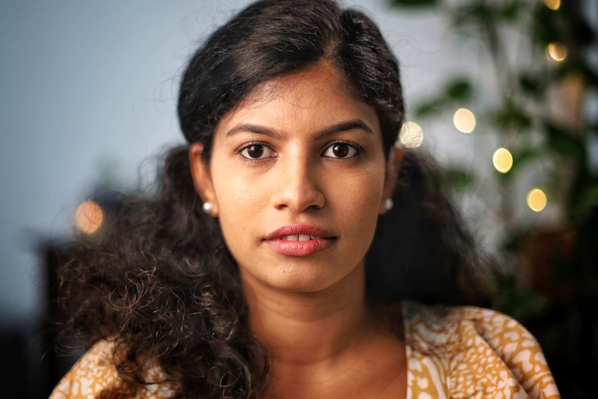 A woman wears a yellow and white top.