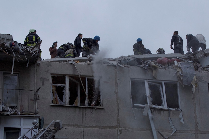Rescuers work on the top of a building damaged in a shelling, with windows blown out. 