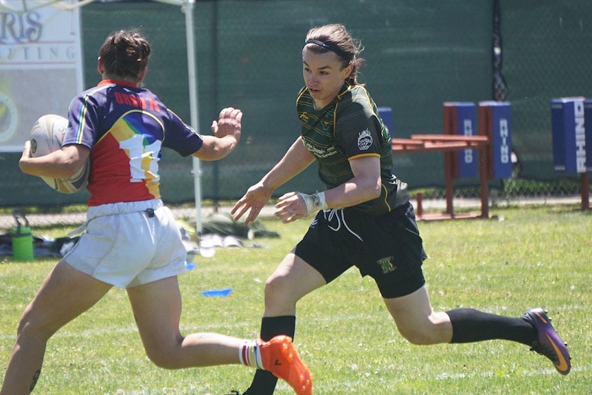 Grace McKenzie in a green jersey about to tackle another rugby player.
