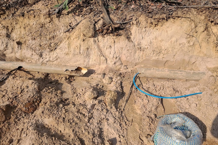 Dry ground showing a plastic pipe broken and a blue cable exposed.