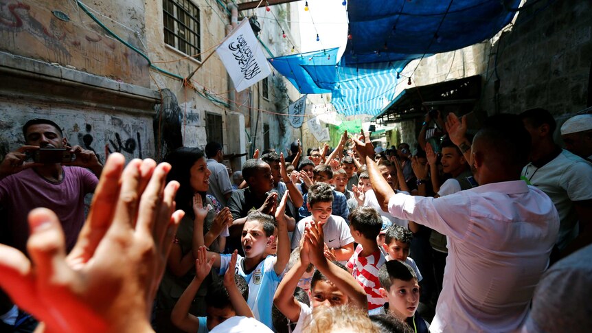 Children and adults celebrate with raised hands in a street in Jerusalem after the announcement.