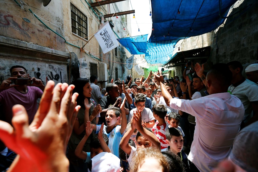 Children and adults celebrate with raised hands in a street in Jerusalem after the announcement.