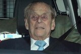 Prince Philip stares ahead as he sits in the car. His seatbelt is secured, and there is a man in a tweed jacket behind.