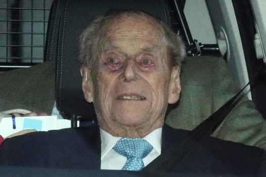 Prince Philip stares ahead as he sits in the car. His seatbelt is secured, and there is a man in a tweed jacket behind.