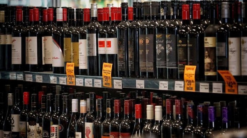 Many bottles of red wine on shelf in bottle shop.