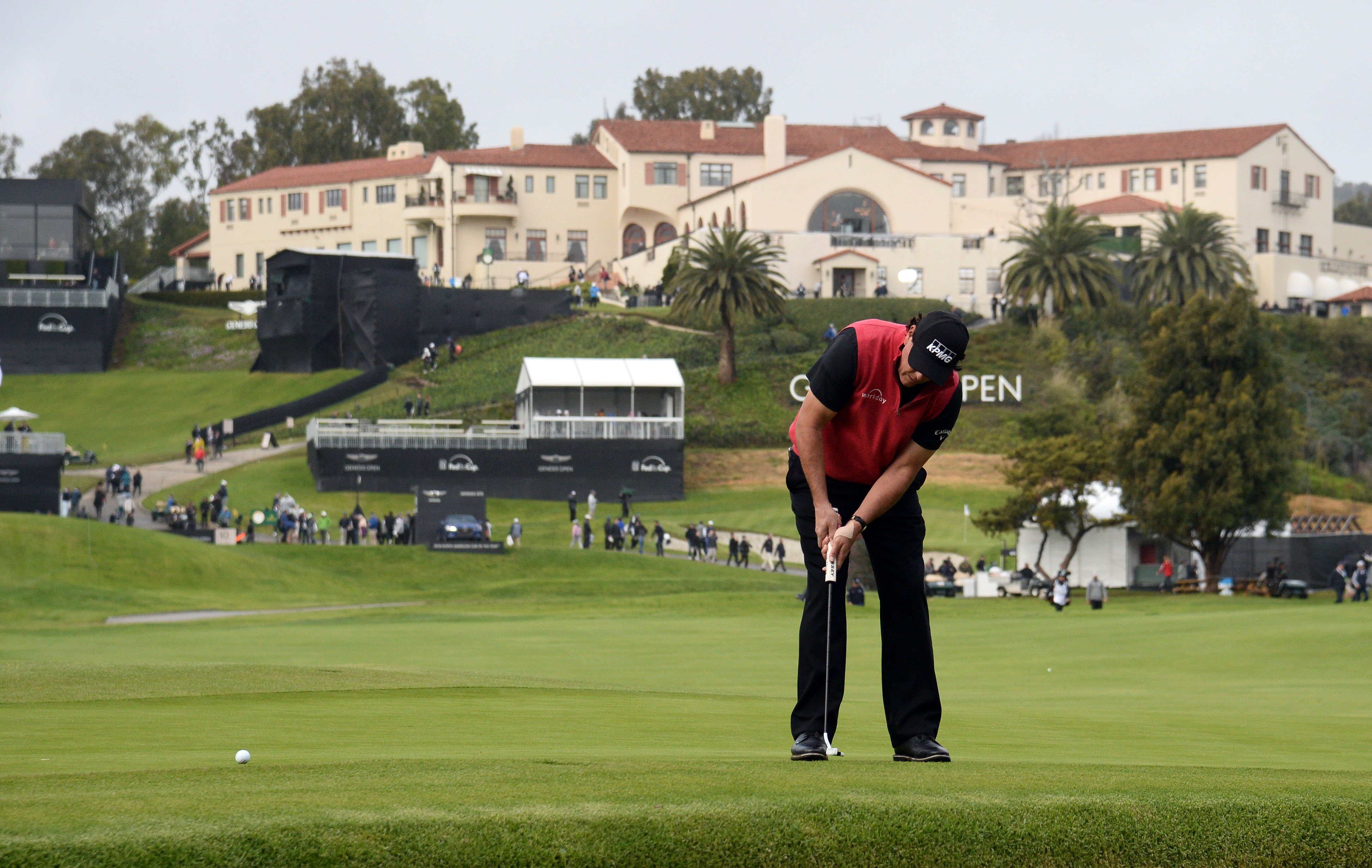 A golfer putts as the sprawling Riviera Country Club stands on a green hill in the background