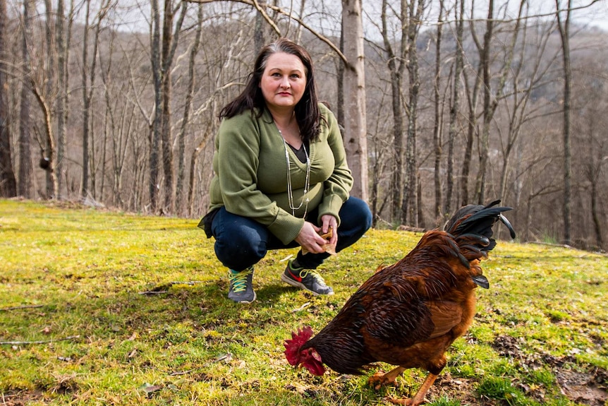 A woman crouching in the grass next to a rooster