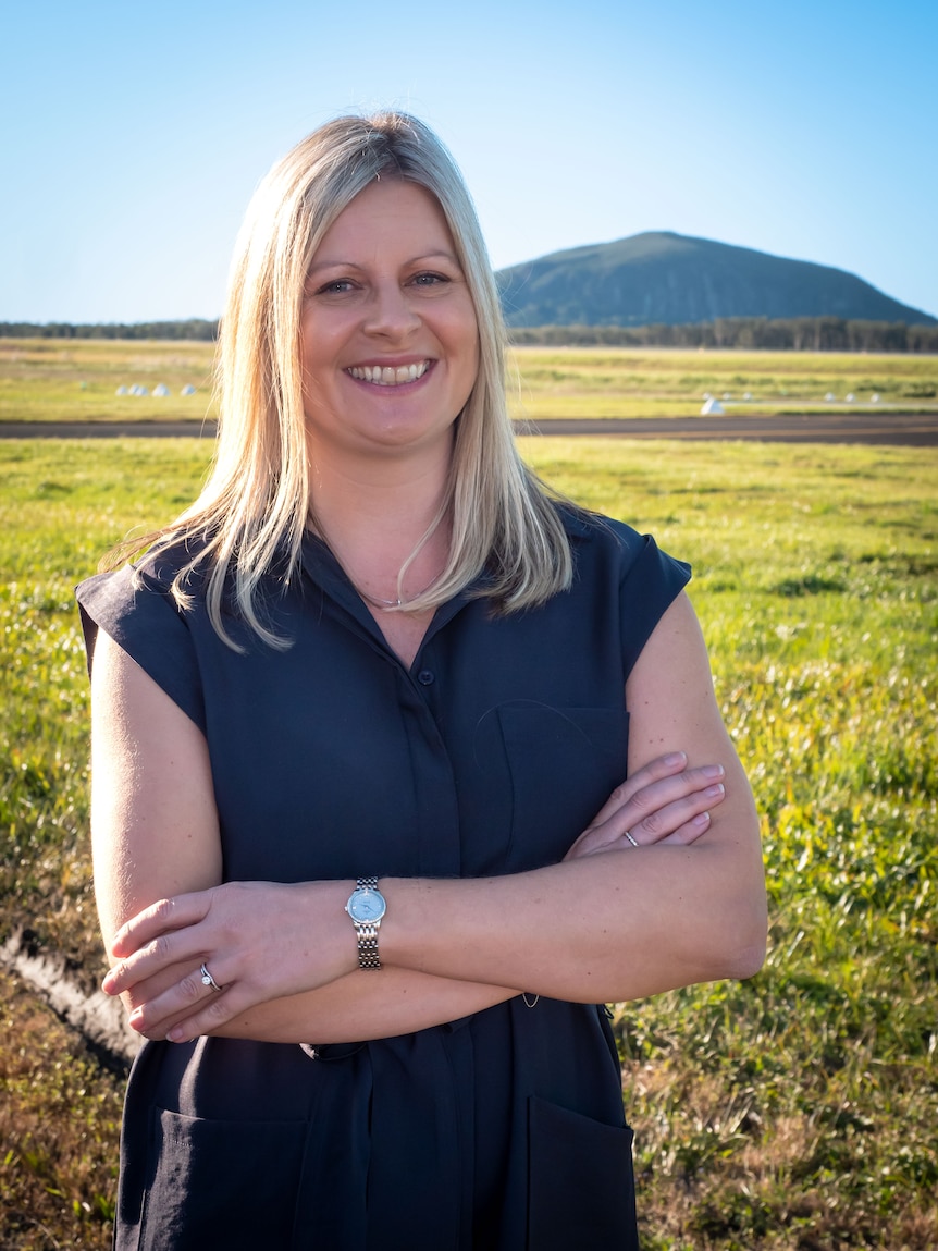 Woman in black t-shirt smiling at camera, with Mount Coolum behind her.