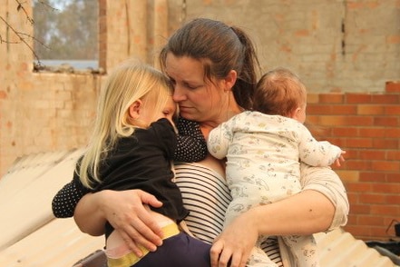 A woman holding her two children in the burnt-out rubble of a house.