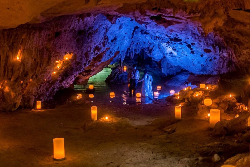 Candles light an underground cave with shallow water in it.