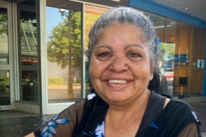 Beverley Roberts sits outside at a table and smiles at the camera.