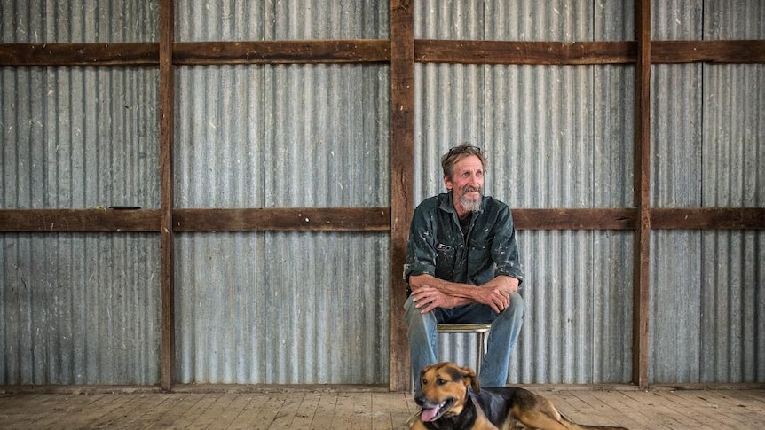 A man sits in a tin shed with his dog.