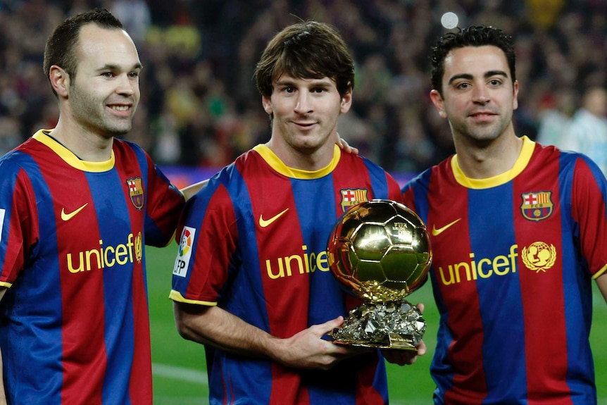 Lionel Messi shows off one of his five Ballon d'Or trophies alongside Andres Iniesta and Xavi