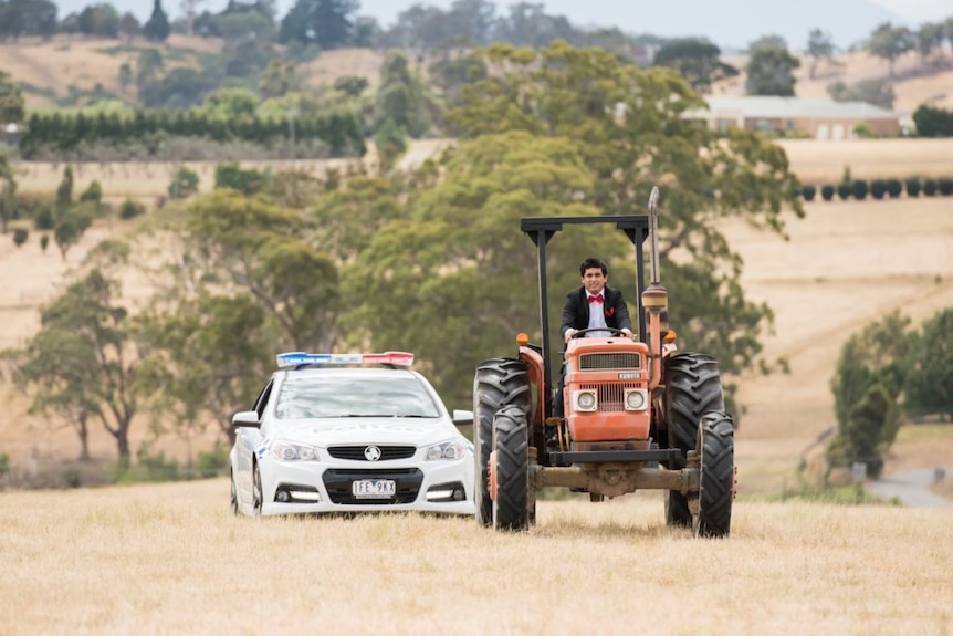 Still image from 2017 film Ali's Wedding, a police car tails actor Osamah Sami as he drives a farm tractor through a field.