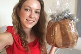A selfie of a young woman in red dress holding a panettone in bed