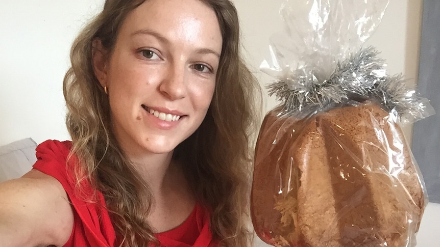 A selfie of a young woman in red dress holding a panettone in bed