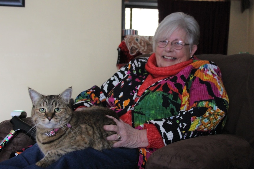 A woman sitting with a cat in her lap smiles at the camera
