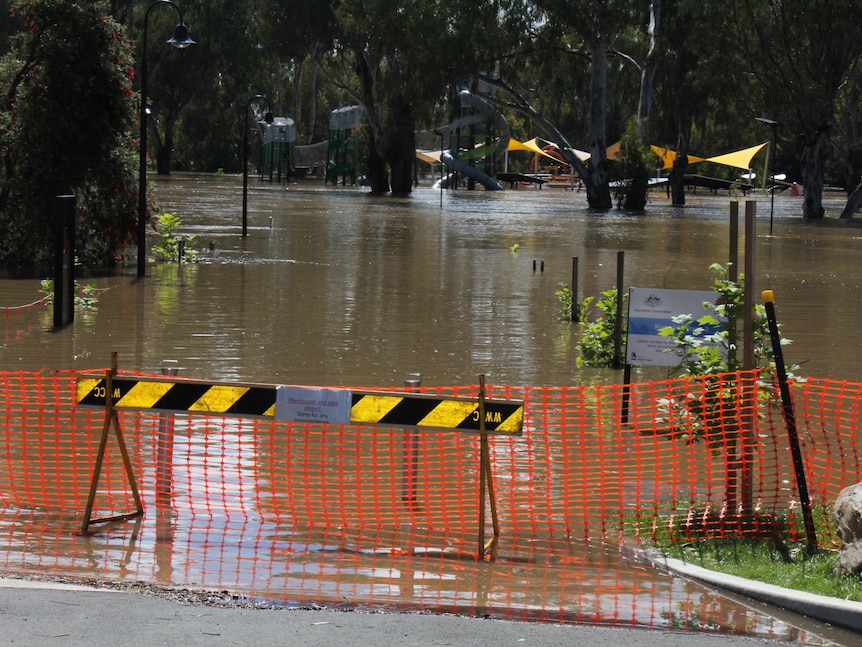 An orange fence in front of floodwater and a children's playground near the Murrumbidgee River at Wagga Wagga.
