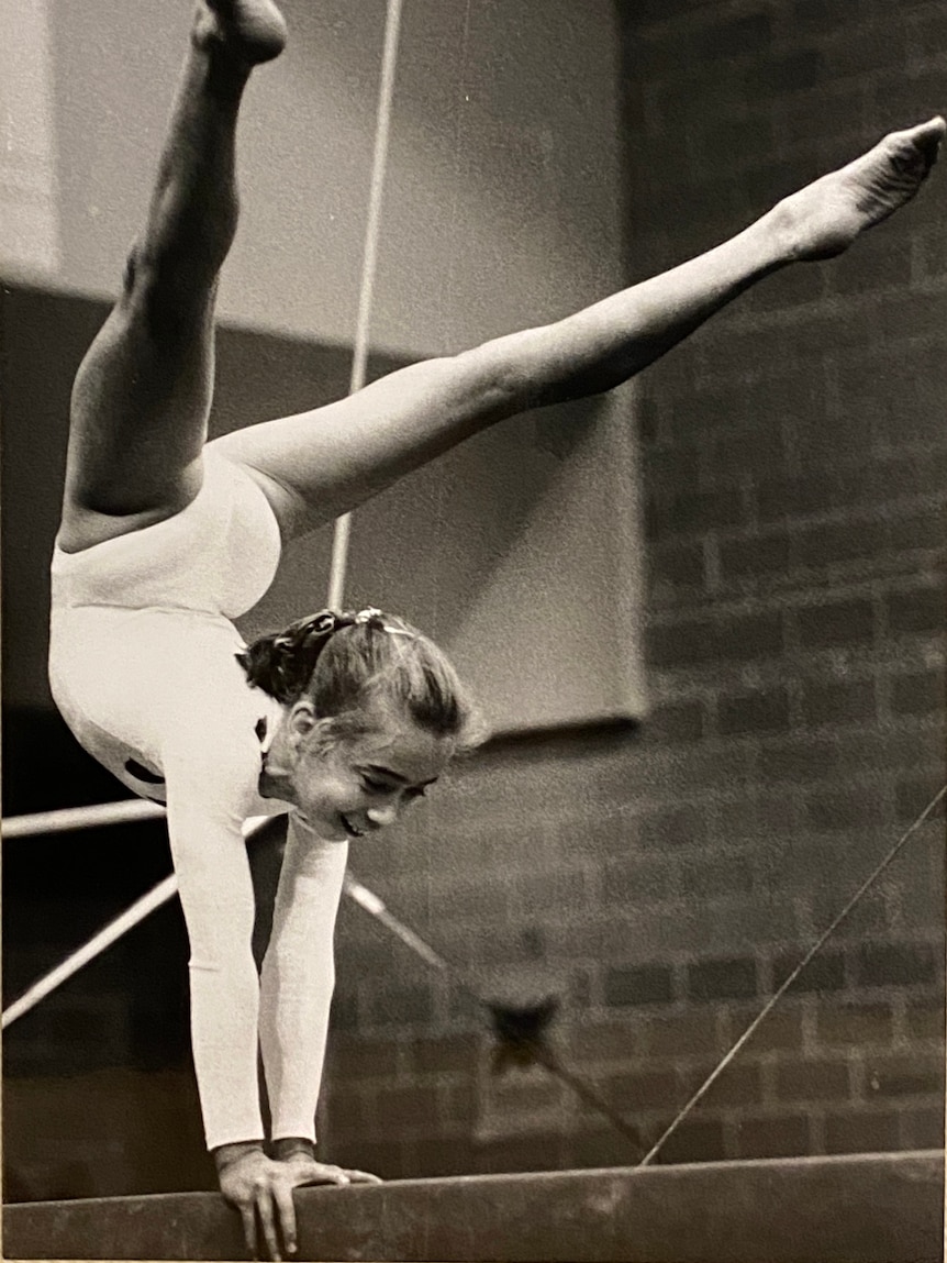 Black and white picture of a young gymnast balancing on her hands on a beam.