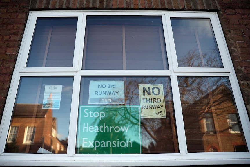 Signs behind a window say "Stop Heathrow Expansion" and "No third runway".
