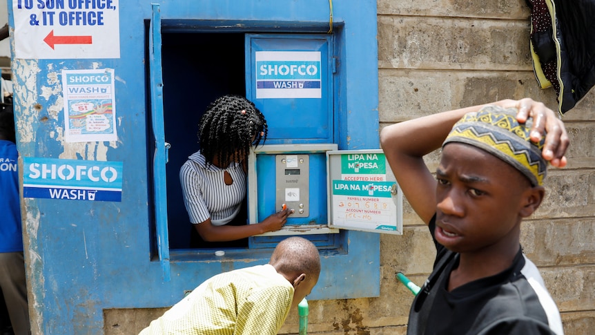 Woman puts money into the slot of a machine installed in a wall in Kenya 