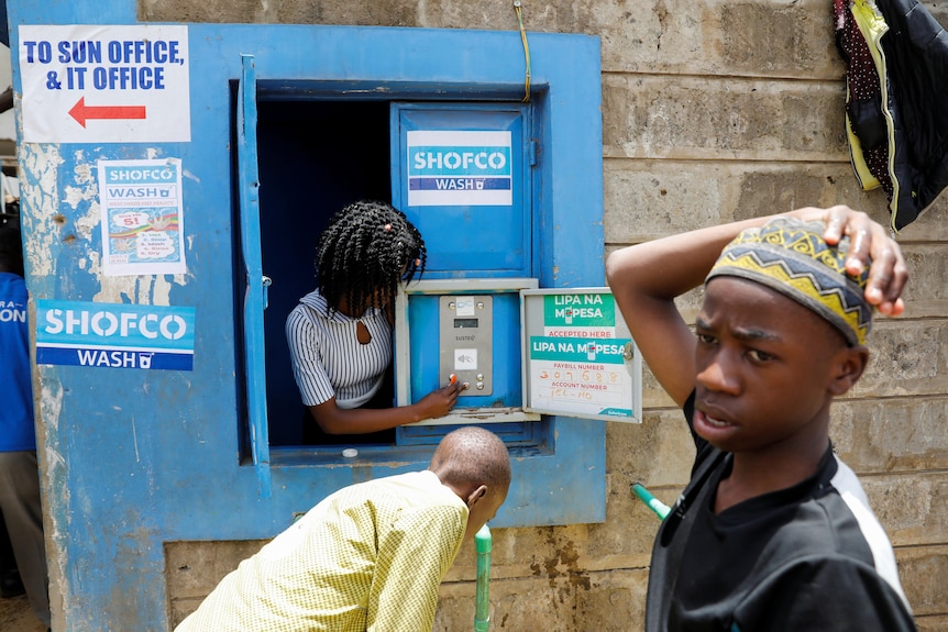 Woman puts money into the slot of a machine installed in a wall in Kenya 