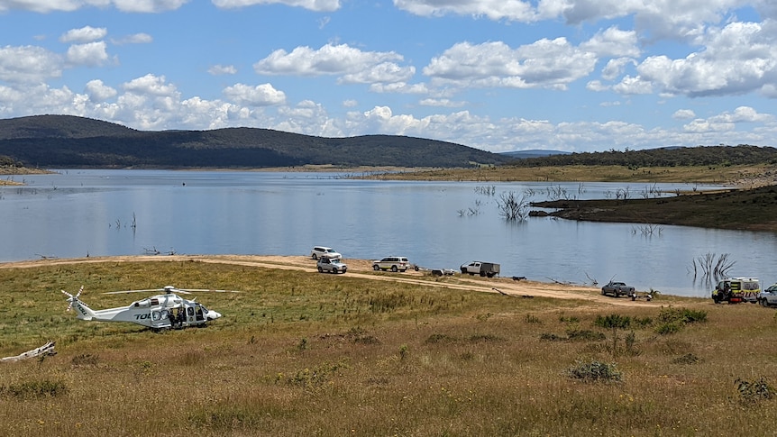 the picture of a lake with a helicopter and ambulance in the foreground