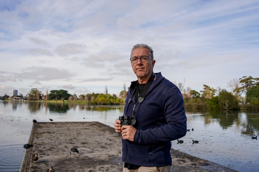 A man holding binoculars near a lake
