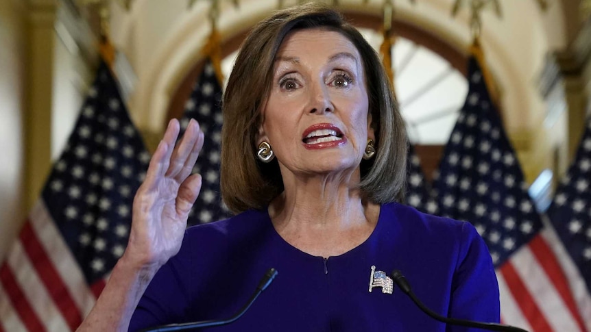 Nancy Pelosi gestures as she gives a speech in front of flags