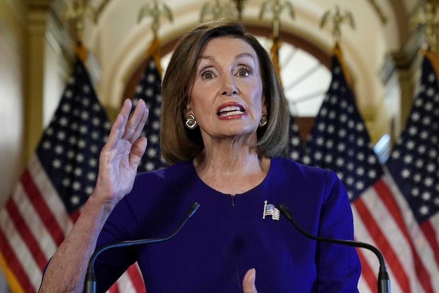 Nancy Pelosi gestures as she gives a speech in front of flags