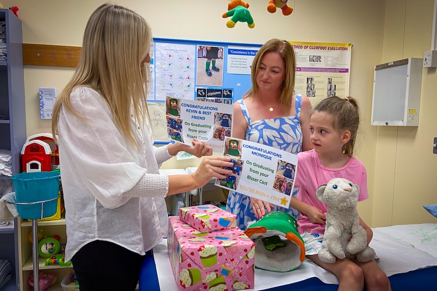 A young girl receives presents and a certificate from a woman with blonde hair.