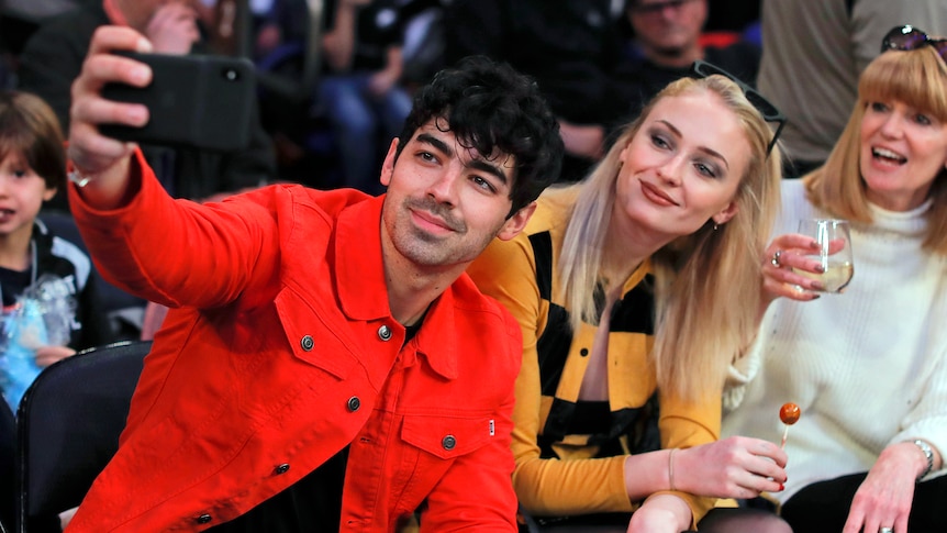 Man wearing a jacket holding out a phone to take a photo with the lady behind him